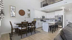 Kitchen with appliances with stainless steel finishes, a breakfast bar, a kitchen island with sink, white cabinets, and a high ceiling