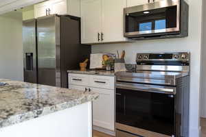 Kitchen with stainless steel appliances, white cabinets, and light stone countertops