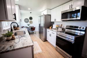 Kitchen featuring appliances with stainless steel finishes, light stone counters, light wood-style flooring, white cabinetry, and recessed lighting