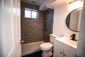 Full bath featuring vanity, a tile shower, and dark tile patterned flooring
