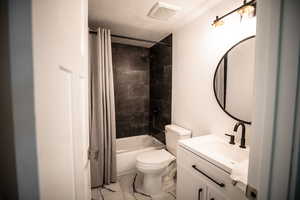 Full bathroom featuring shower / bath combo with shower curtain, a textured ceiling, vanity, and light marble finish flooring