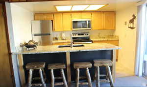 Kitchen featuring stainless steel appliances, light brown cabinets, and a breakfast bar area