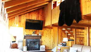 Living area with vaulted ceiling, wooden walls, a fireplace with raised hearth, and stairs