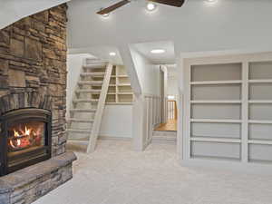 Unfurnished living room featuring light colored carpet, ceiling fan, a stone fireplace, recessed lighting, and stairway