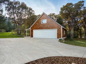 Detached garage, concrete driveway, and view of wooded area.