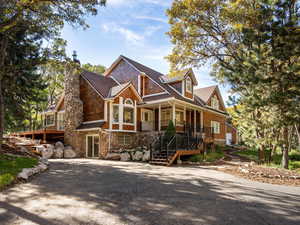 View of front of property featuring stairs, covered porch, a chimney, and stone siding