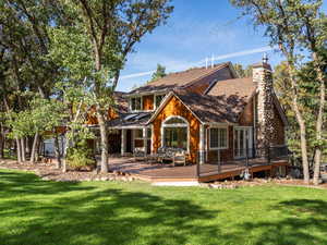 Rear view of property featuring a wooden deck, a lawn, and a chimney