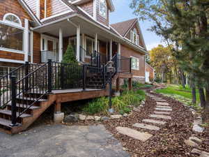 View of property exterior with a shingled roof, a porch, and stairway