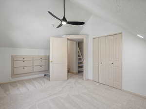 Upstairs bedroom with lofted ceiling, light colored carpet, a textured ceiling, and a ceiling fan
