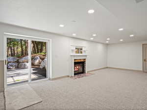Basement living room with light carpet, recessed lighting, and a high end fireplace.