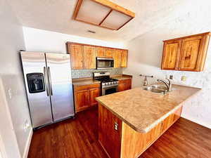 Kitchen featuring a textured wall, a textured ceiling, stainless steel appliances, brown cabinets, and a peninsula
