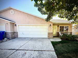 Ranch-style house featuring stucco siding, driveway, stone siding, and an attached garage