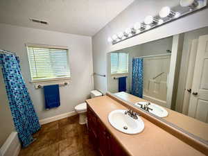 Bathroom featuring vanity, a textured ceiling, shower / bath combo with shower curtain, and dark tile patterned floors