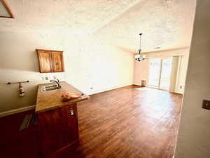 Unfurnished dining area with a textured wall, a textured ceiling, dark wood-style floors, a chandelier, and vaulted ceiling