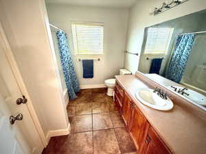 Bathroom with shower / bath combo with shower curtain, vanity, and dark tile patterned flooring