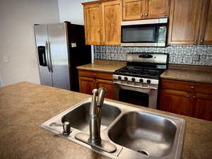 Kitchen featuring brown cabinets, stainless steel appliances, tasteful backsplash, and a textured wall