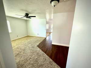 Carpeted spare room with a textured ceiling, wood finished floors, and a ceiling fan
