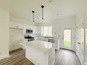 Kitchen featuring white cabinetry, appliances with stainless steel finishes, a kitchen island, light stone countertops, and hanging light fixtures