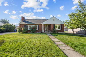 View of front of property with brick siding, a front yard, a chimney, and a shingled roof