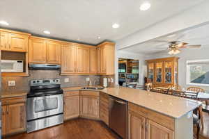 Kitchen featuring appliances with stainless steel finishes, decorative backsplash, light stone countertops, dark wood-type flooring, and a peninsula