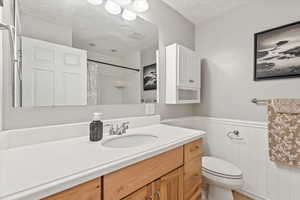 Full bathroom with vanity, a textured ceiling, wainscoting, and a shower with curtain