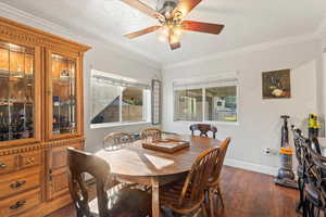 Dining area featuring dark wood-style floors, crown molding, plenty of natural light, and a ceiling fan