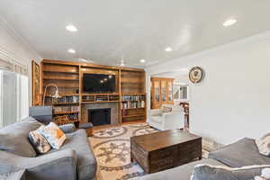 Living room with ornamental molding, recessed lighting, built in shelves, a tiled fireplace, and wood finished floors