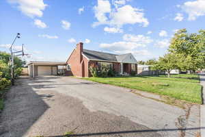 Ranch-style home featuring a front yard, a chimney, brick siding, an outbuilding, and a garage