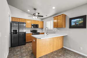 Kitchen featuring refrigerator with ice dispenser, light countertops, a peninsula, black electric range oven, and brown cabinets