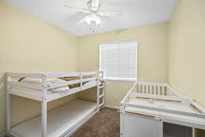 Bedroom with dark colored carpet, a ceiling fan, and a crib
