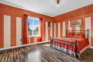 Bedroom with wood finished floors, lofted ceiling, and wallpapered walls