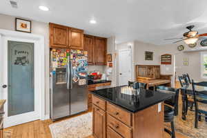 Kitchen with brown cabinetry, stainless steel fridge, light wood-style floors, a center island, and a breakfast bar area