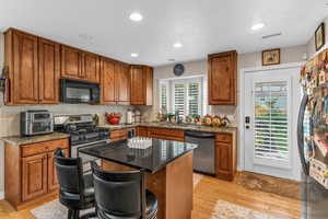 Kitchen featuring decorative backsplash, brown cabinets, dark stone countertops, a kitchen island, and stainless steel appliances