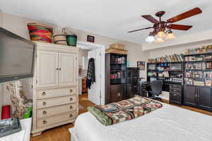 Bedroom featuring light wood finished floors, an office area, and a ceiling fan