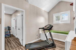 Workout area featuring vaulted ceiling and dark wood-type flooring