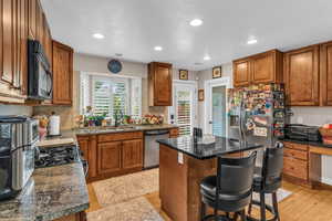 Kitchen with brown cabinetry, a kitchen island, a breakfast bar area, stainless steel appliances, and recessed lighting