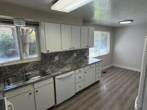 Kitchen with tasteful backsplash, white cabinets, dark countertops, white appliances, and a textured ceiling