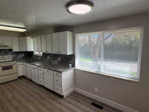 Kitchen featuring white appliances, a textured ceiling, white cabinetry, backsplash, and dark wood finished floors