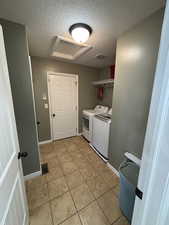 Laundry room with a textured ceiling, attic access, washer and dryer, and light tile patterned floors