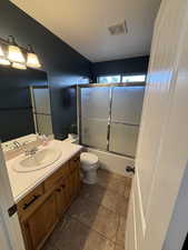 Full bath featuring vanity, shower / bath combination with glass door, a textured ceiling, and light tile patterned floors