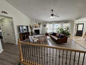 Living room featuring vaulted ceiling, a fireplace with raised hearth, a textured ceiling, dark wood-type flooring, and a ceiling fan