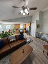 Living room with vaulted ceiling, ceiling fan, a textured ceiling, light wood finished floors, and a chandelier