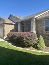 View of side of home featuring stone siding, an attached garage, and a yard