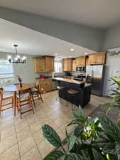 Kitchen with a breakfast bar area, stainless steel appliances, light tile patterned floors, a center island, and a chandelier