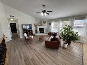 Living room featuring a glass covered fireplace, vaulted ceiling, wood finished floors, a textured ceiling, and ceiling fan