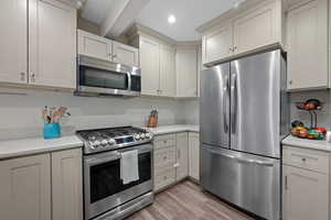 Kitchen featuring stainless steel appliances, light wood-type flooring, light stone counters, and white cabinetry