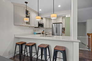 Kitchen featuring a breakfast bar area, appliances with stainless steel finishes, light stone counters, dark wood-style flooring, and a peninsula