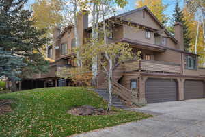 View of front of house with stairs, an attached garage, a front lawn, a balcony, and a chimney