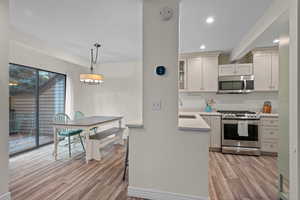 Kitchen with appliances with stainless steel finishes, a breakfast bar area, glass insert cabinets, a peninsula, and recessed lighting