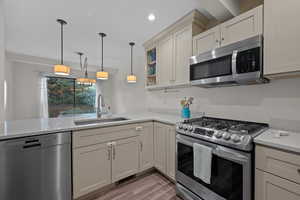 Kitchen with stainless steel appliances, decorative light fixtures, light stone counters, a peninsula, and light wood-style flooring